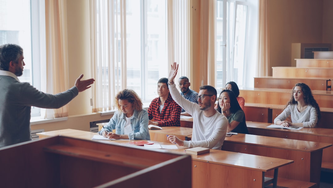 Students raising hands in a lecture hall classroom.